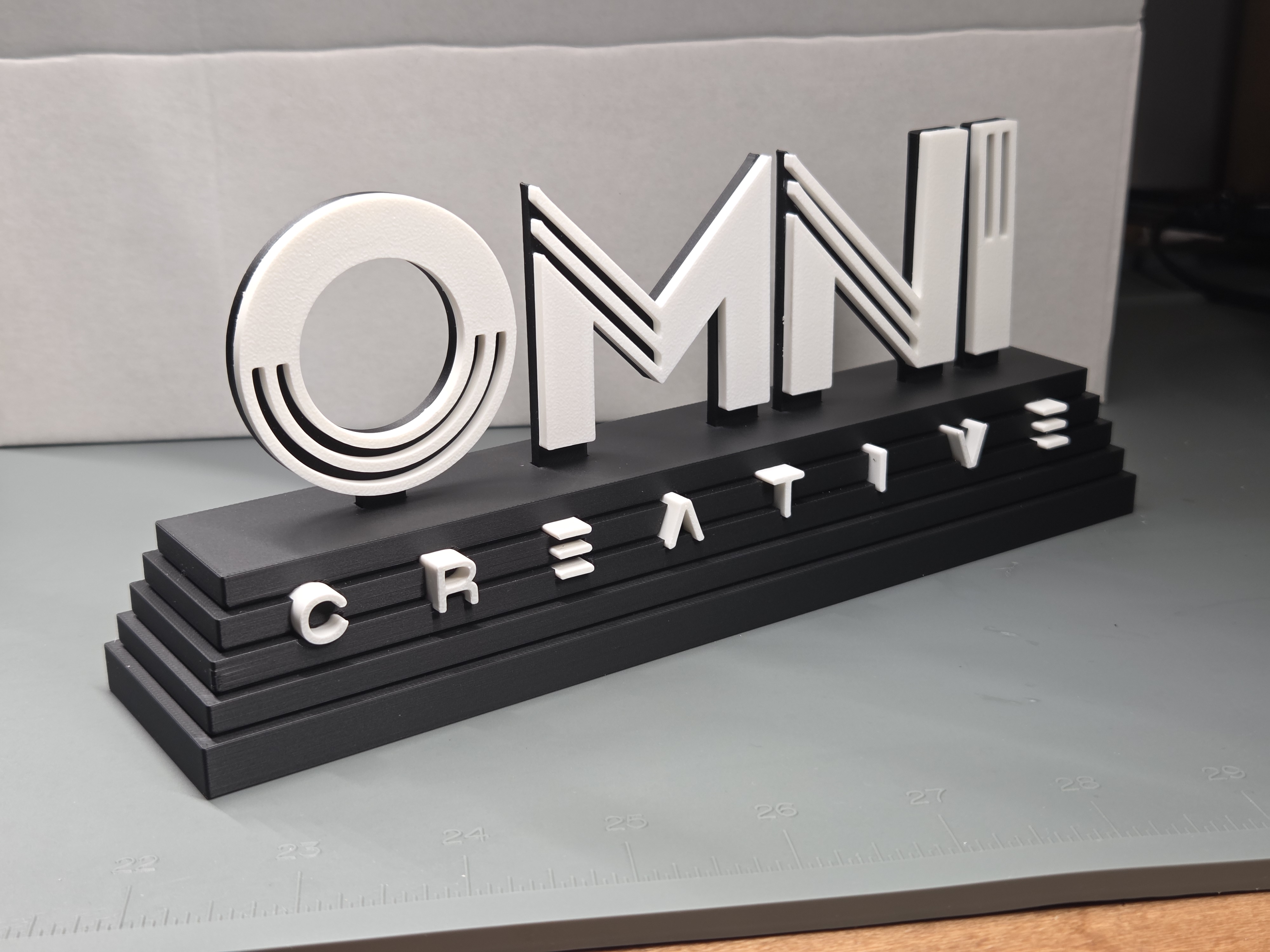 OMNI Creative two-tone logo display piece with raised standoff lettering on a tiered black base